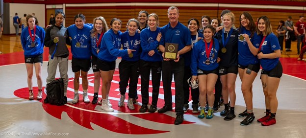 A group photo of the women's wrestling team, Kevin Pine presents an award in the center