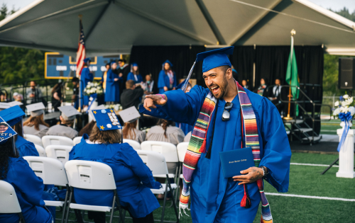 Un estudiante graduado sonríe y señala al grupo de personas después de recibir su diploma.