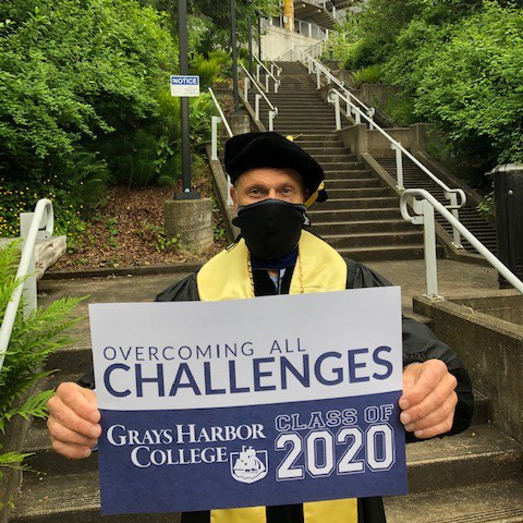 Dr. Minkler holding a graduation sign while standing in front of the college