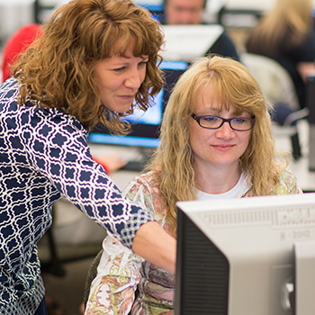 A person giving a student some assistance on a computer