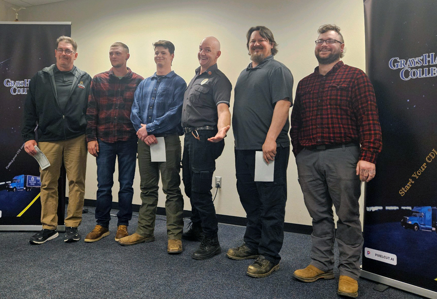 Six students grin for the camera in an angled line. One in the middle splays his arms in a dramatic pose for the camera, while the rest are casual.