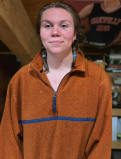 Carmella Smiles for a casual photo. Her hair is put back in double braids and she is wearing an oversized tracksuit jacket.