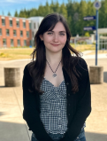 Eva smiles for a headshot on the GHC campus. She's wearing a black cardigan and checkered top.