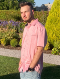 Justin Pop stands at a 3/4 angle facing the sun, behind him are various topiaries.