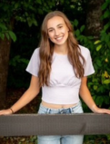Samantha poses infront of a handrail. She is weaing a white T-shirt and light wash skinny jeans.