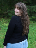 Sophie sends a smile to the camera over her shoulder. She is surrounded by greenery.