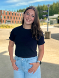 Willobelle stands for a photo on the GHC campus. She is wearing a black T-shirt and bright blue jeans. 