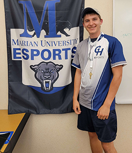Andrew Burkhart standing in front of a Marian University Esports banner