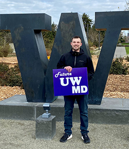 Seth Ronk standing by a W statue holding a sign reading future UW MD