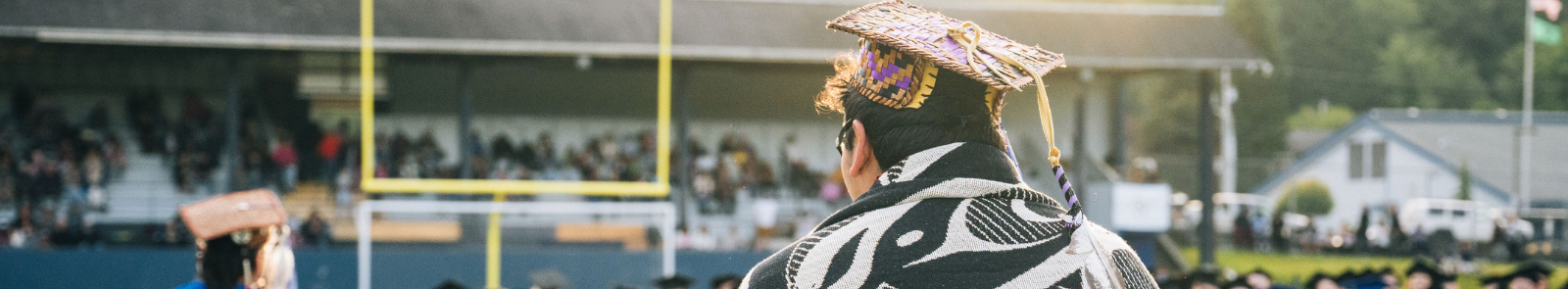 A graduate with native woven cap and blanket stands before the crowd on graduation day.