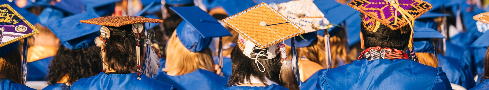 The backs of a crowd of GHC graduates. Mixed in with the college's signature blue caps and robes are woven caps.