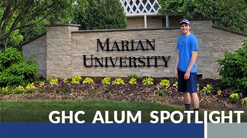 Andrew Burkhart standing in front of a sign for Marian University - GHC Alum Spotlight