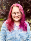 Kailei Smiles for a casual headshot. She is wearing a light blue camo hoodie that compliments her bright pink hair.