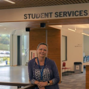 Shelly Hoffman leaning on a railing in front of the Student Services sign in the tulalW building