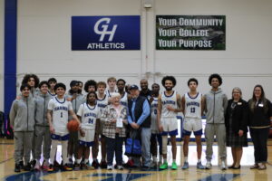 GHC Chokers basketball team stand together on the court with George and Kathy Leach, smiling at the camera.