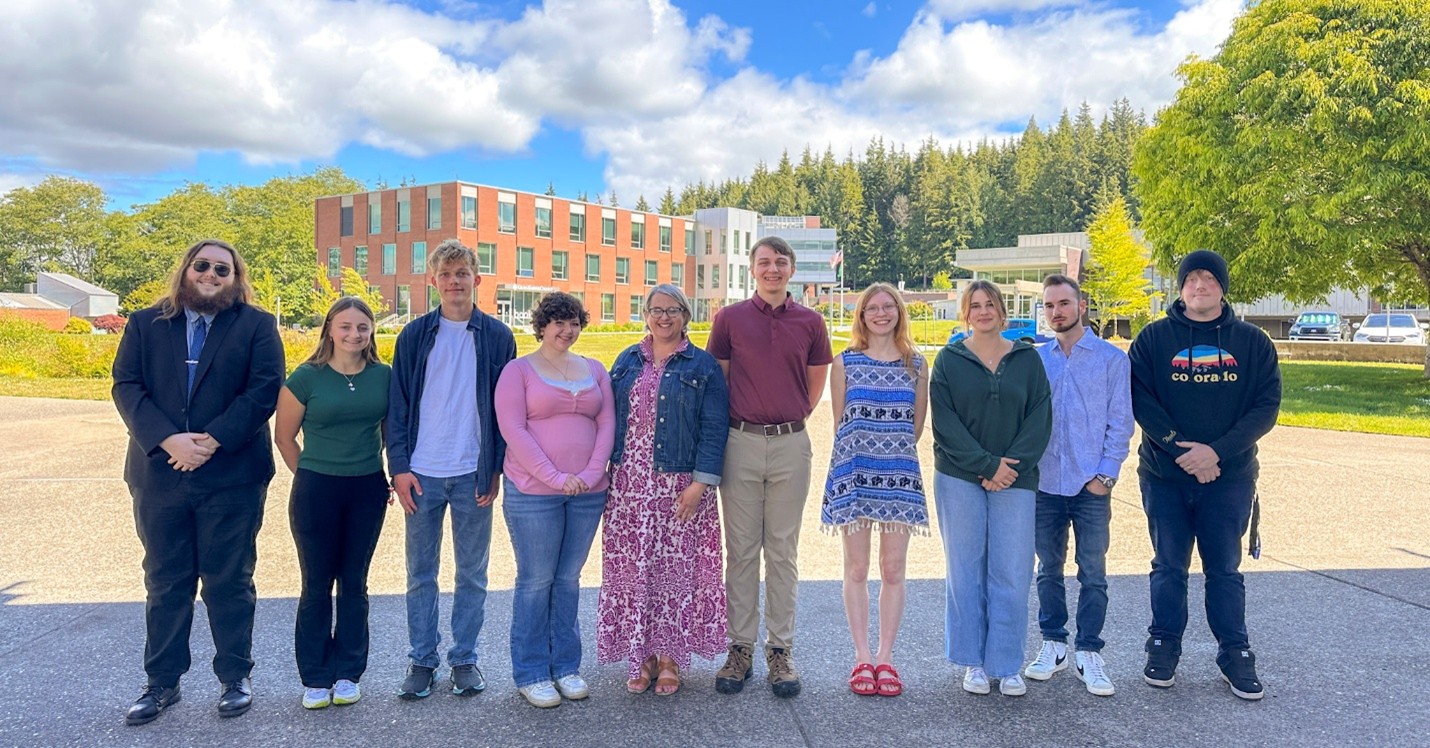GHC Graduates and Carli Schiffner stand at the upper level of the main GHC campus on a sunny day.