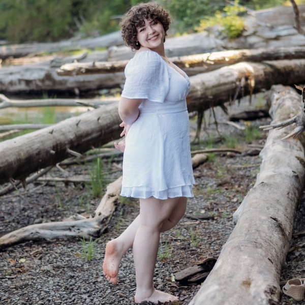 Natalie Wharton standing next to logs on a beach