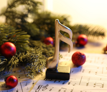 A golden trophy 16th note, in front of red christmas bobbles and the bottom of a christmas tree.