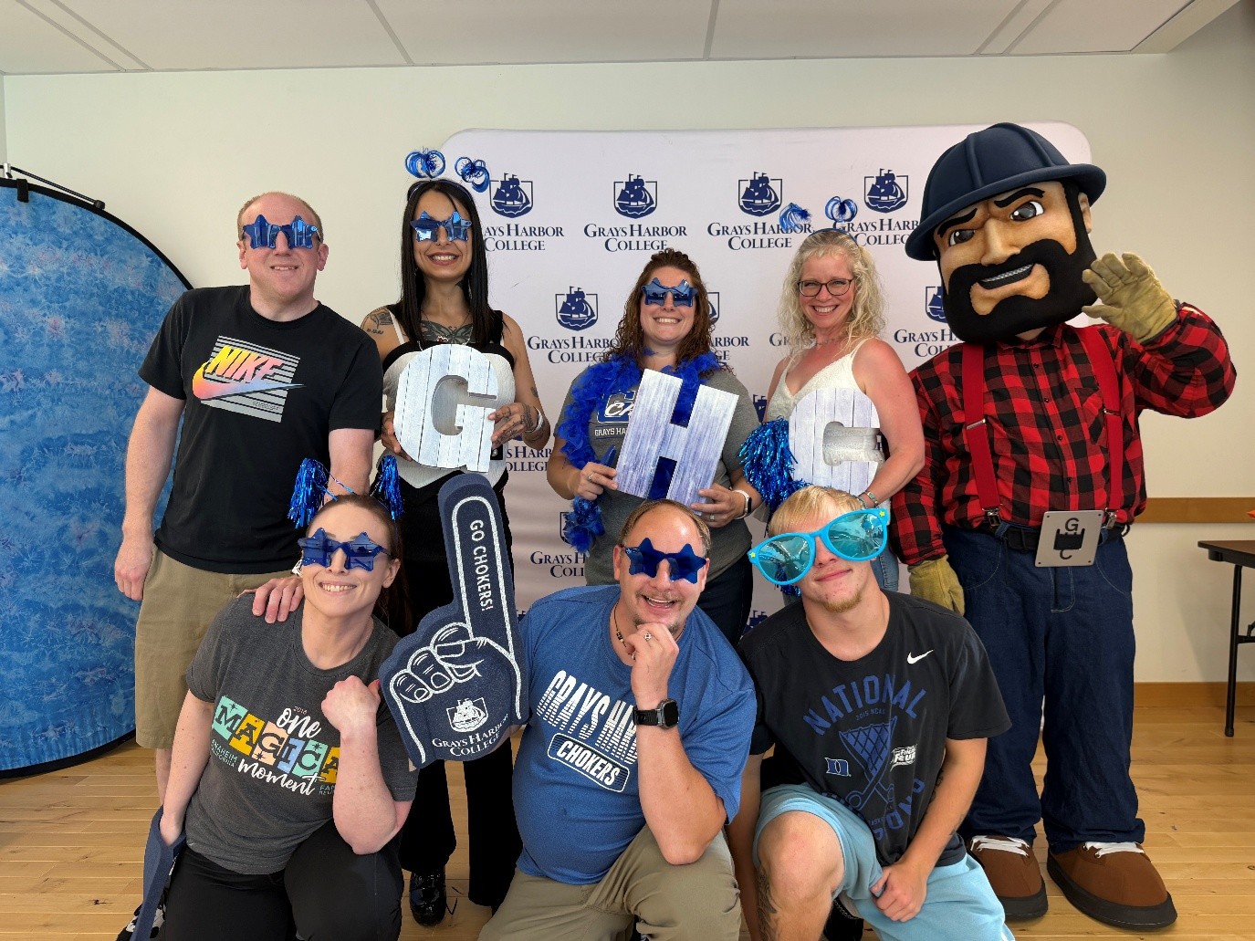 The Student life team and Charlie Choker posed for a photo wearing various GHC memorabilia like blue star sunglasses, pom poms, and GHC signs.