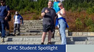 Student Spotlight, Austin Winkle. Austin poses in a black tshirt and shorts, making a 'hang loose' hand sign.