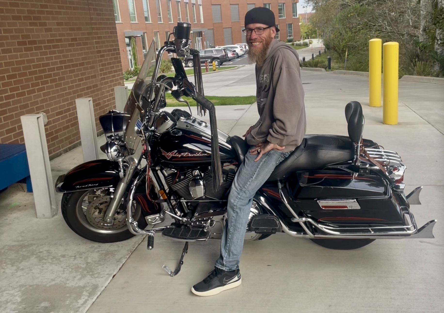 Derek grins widely, sitting on a black motorcycle in one of the GHC parking lots.