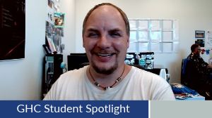 Student Spotlight, Donald Reifenstahl. Donald smiles with squinted eyes for the camera, he wears a wooden necklace and a white t-shirt.