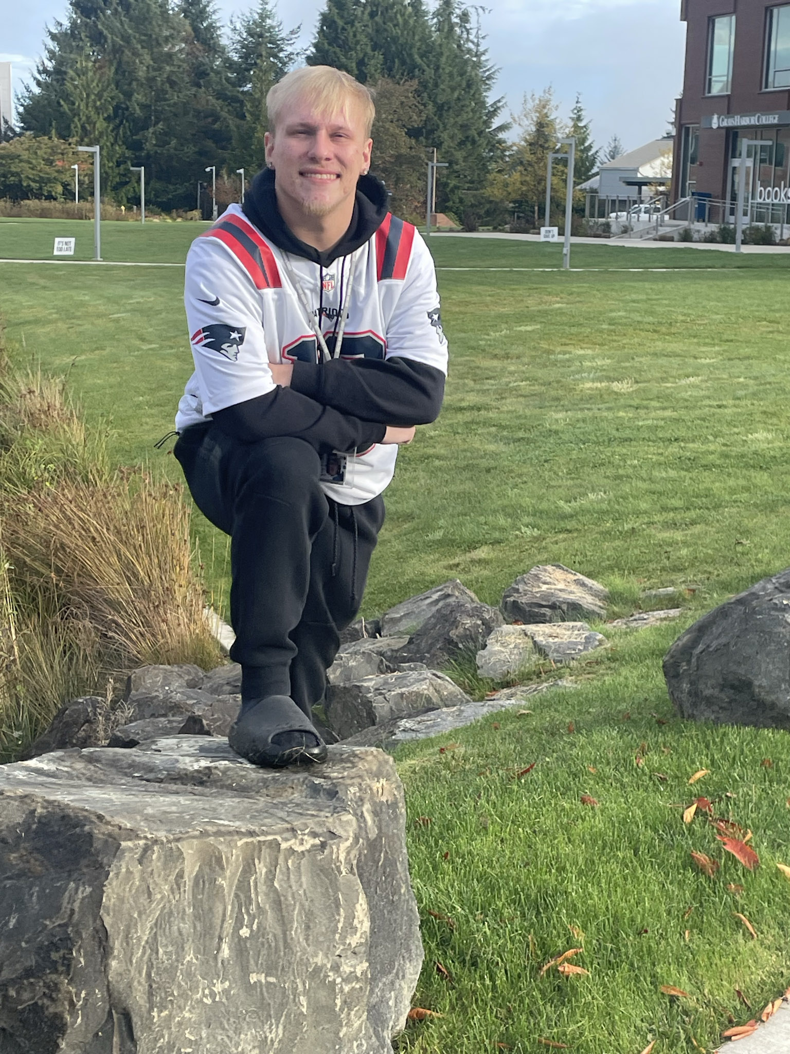 Legend leans half on a rock, arms crossed. Legend wears a sports jersey over a hoodie, though it's hard to make out what team it is for.