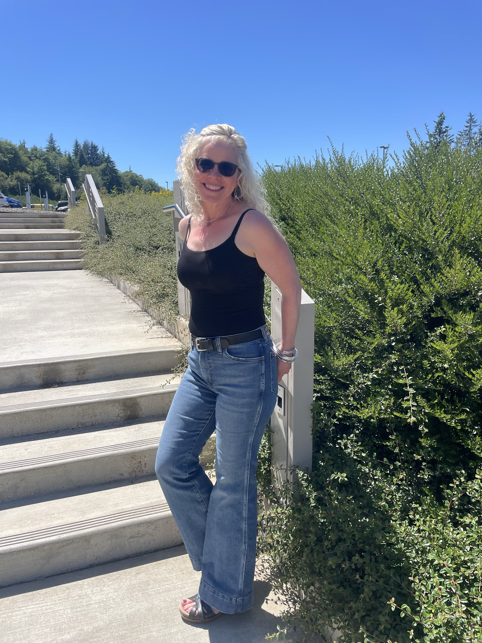 Lisa poses against a stair railing on GHC campus. Lisa is wearing an outfit suited to the sunny blue sky and some sunglasses.